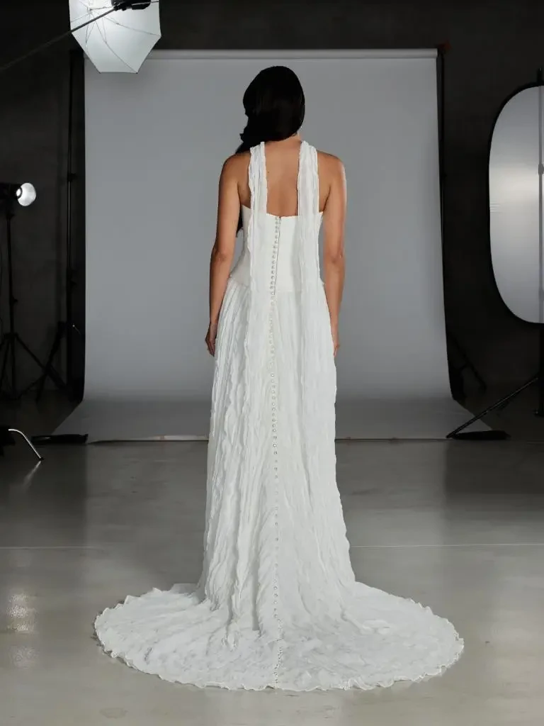Model is wearing a drop-waist wedding gown with a strapless suede satin bodice and pleated chiffon skirt, finished with a matching chiffon neck scarf.