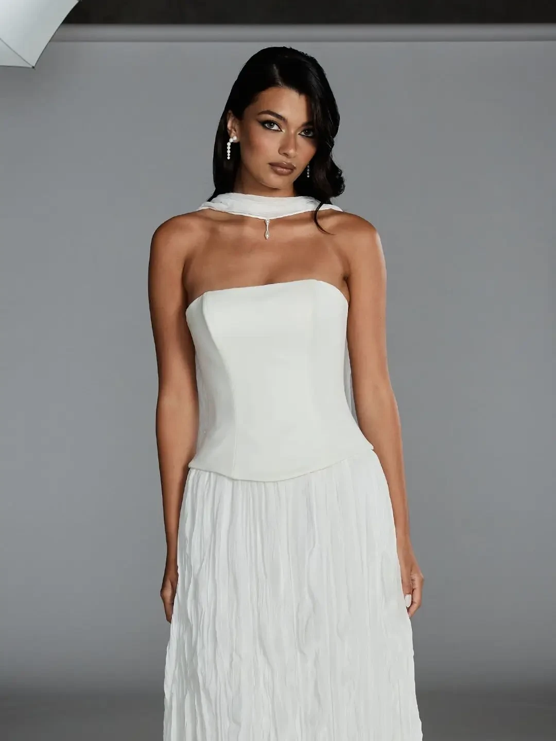Model is wearing a drop-waist wedding gown with a strapless suede satin bodice and pleated chiffon skirt, finished with a matching chiffon neck scarf.