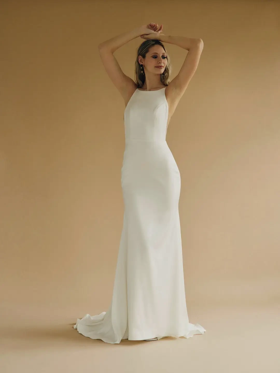 Model is wearing a sleek satin mermaid wedding dress featuring a high neckline in the front and a low open back.