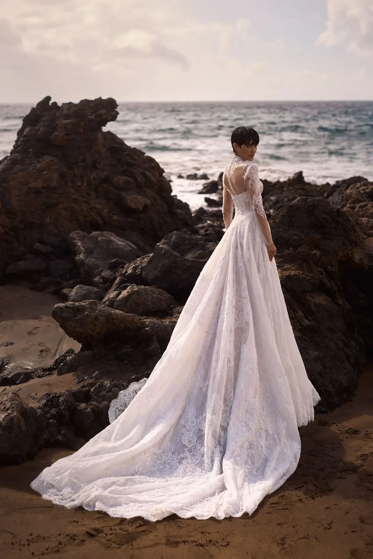 Model is wearing a chantilly lace A-line gown with a heart-shaped neckline, sheer boned corset, and voluminous skirt, styled with an optional long-sleeve bolero and lace choker.