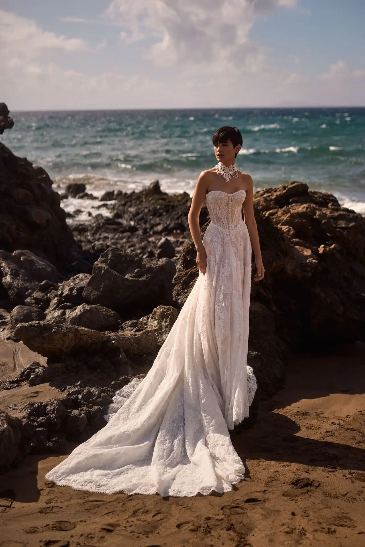 Model is wearing a chantilly lace A-line gown with a heart-shaped neckline, sheer boned corset, and voluminous skirt, styled with an optional long-sleeve bolero and lace choker.