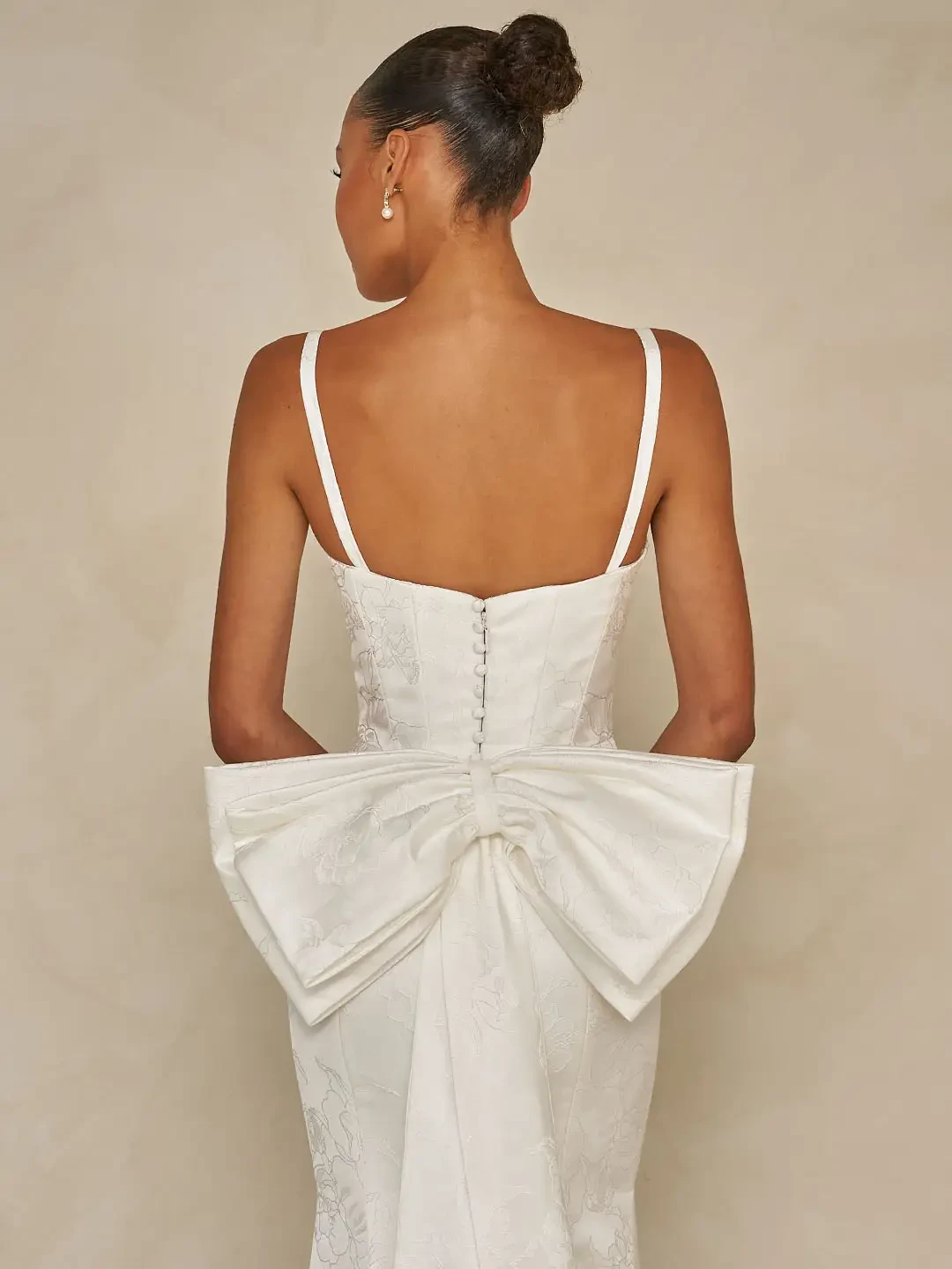 Model is wearing a floral jacquard sheath gown with a square neckline, detachable straps, and an optional A-line overskirt and back bow accessory.