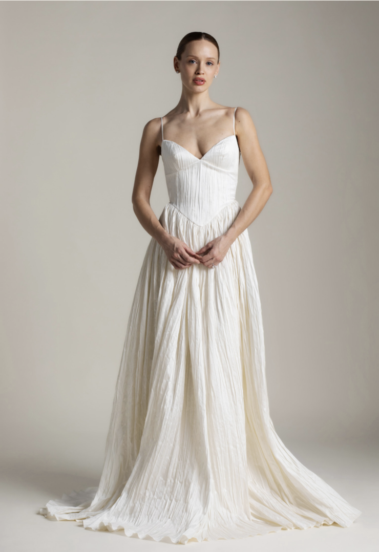A model wearing a long, flowing white dress with thin straps, standing against a neutral background.