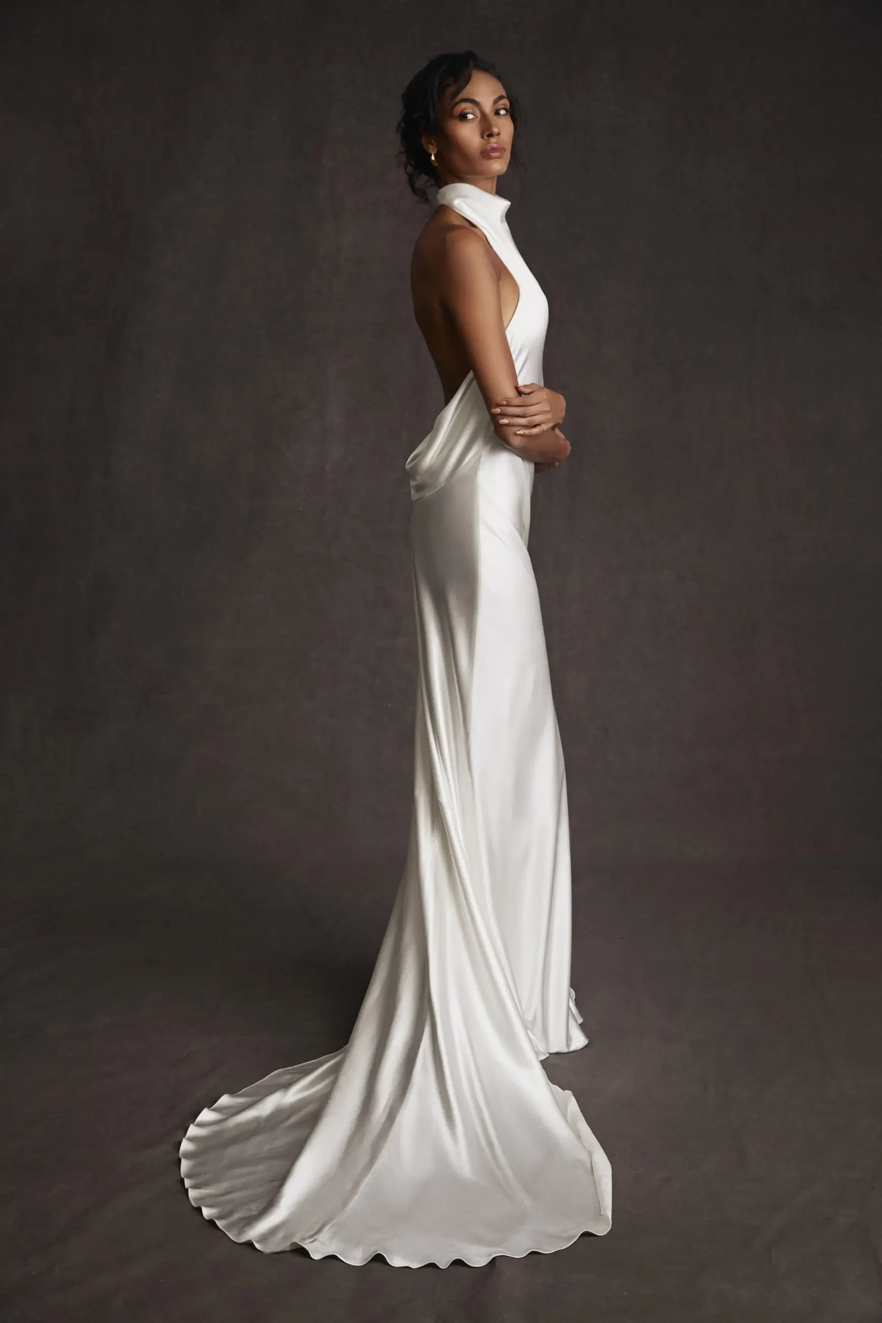 Model is wearing a chic high neck halter wedding dress with an open back