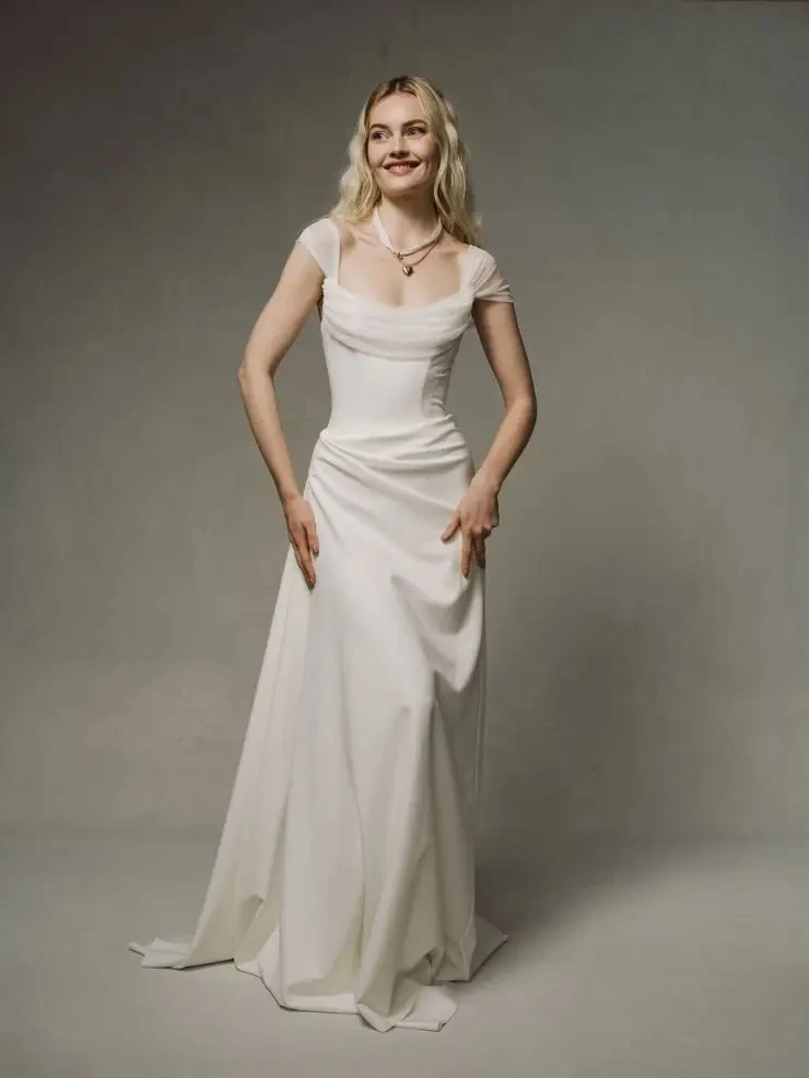 Model is wearing a sheath wedding dress with ruching and delicate cap sleeves