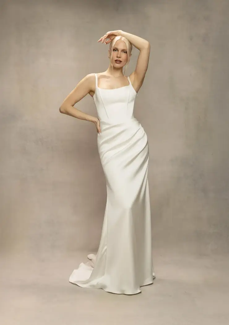 A woman wearing a sleek, white evening gown poses against a neutral backdrop.