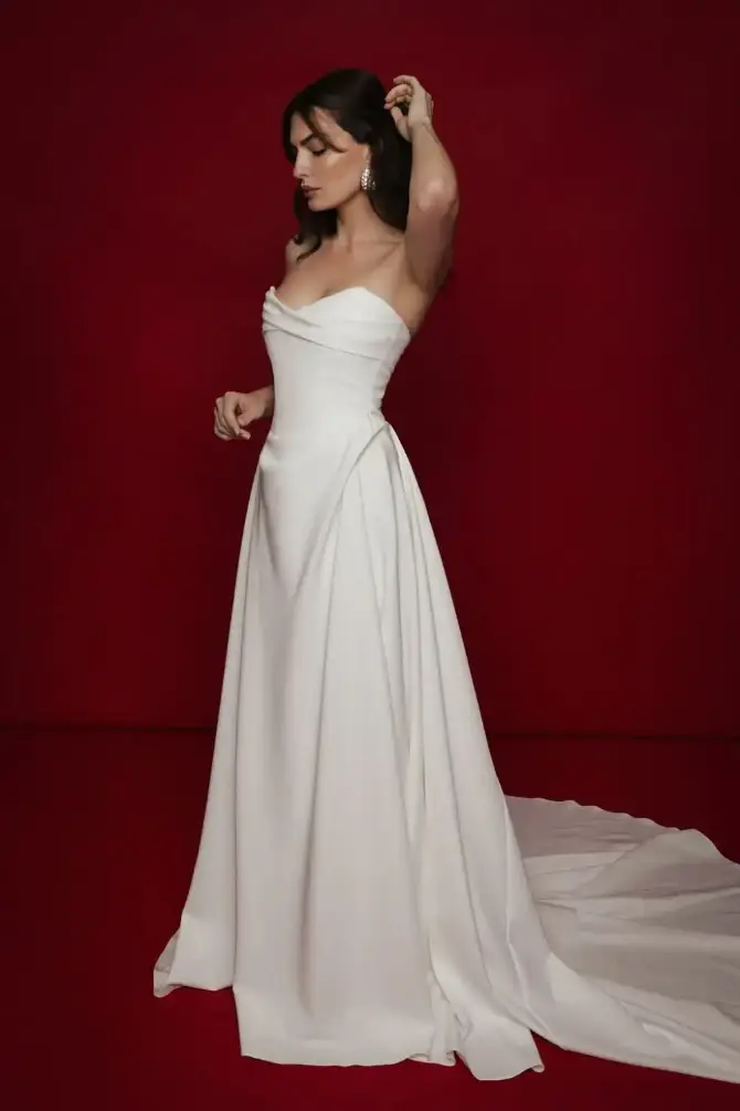 A woman in a strapless white gown poses against a red background.