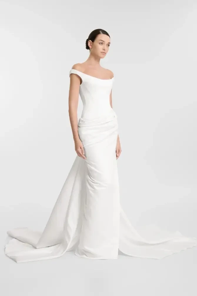 Model is wearing a minimalist sheath bridal gown with off the shoulder straps